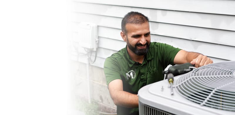 Technician in green uniform working on outdoor AC unit
