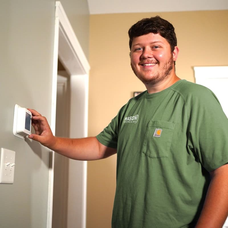 Smiling technician adjusting wall thermostat in a home