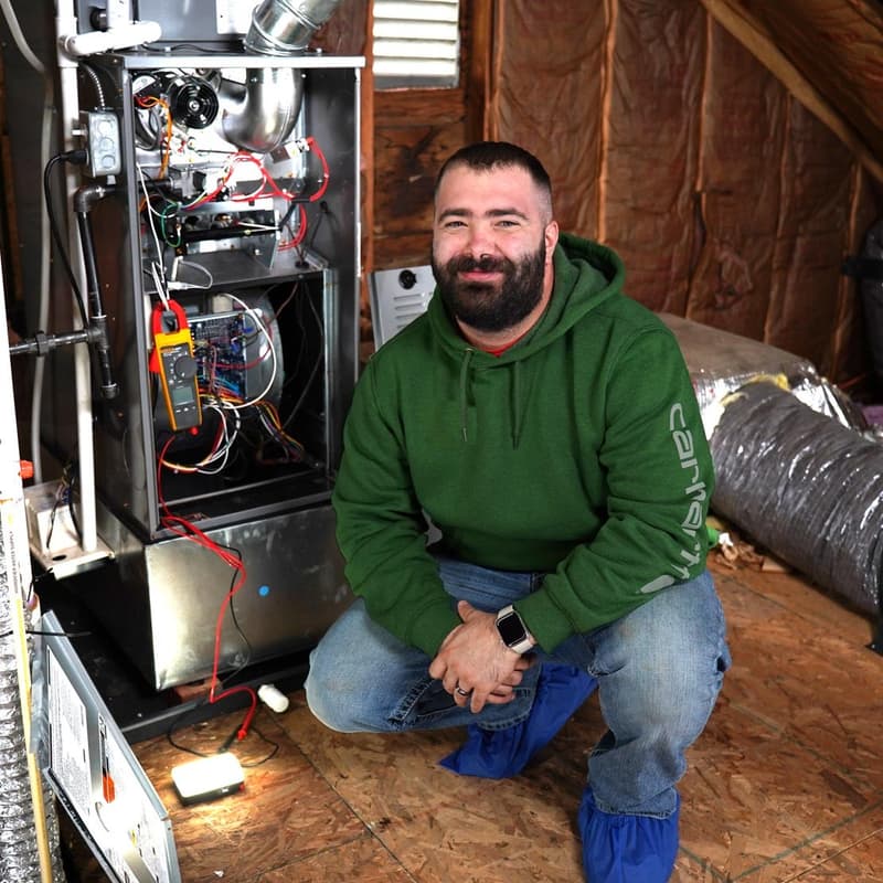 Technician kneeling beside furnace in attic